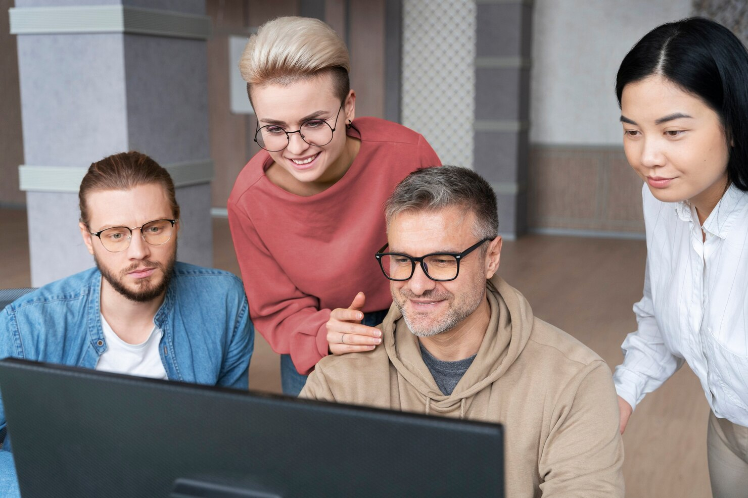 A group of four people gather behind a laptop as they look intently at the screen.